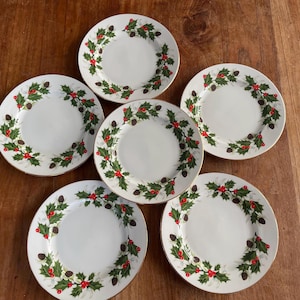 Op de afbeelding: Set van zes witte keramische dinerborden met een groen hulst- en rood bessenontwerp. De borden hebben een gouden rand.