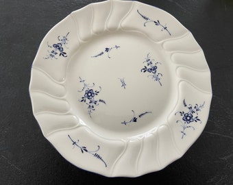 May include: White ceramic plate with a scalloped edge and blue floral designs. The plate has a wavy rim and a center well.