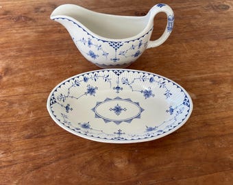 May include: A white porcelain gravy boat and oval serving dish with blue floral patterns. The gravy boat has a handle and spout. The serving dish has a scalloped edge. Both pieces are on a wooden surface.