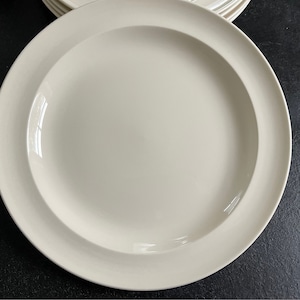Puede incluir: Un plato de cerámica blanco con un borde ligeramente elevado. El plato es liso y tiene un acabado liso y brillante.