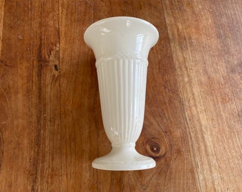 May include: A white ceramic vase with a fluted design. The vase has a wide mouth and a narrow base.