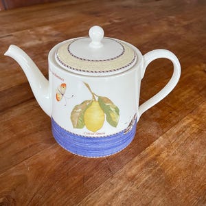 Puede incluir: Tetera blanca con un diseño floral azul y blanco con un limón y una mariposa. La tetera tiene una tapa y un asa. El texto "Citrus Limon" está impreso en la tetera.