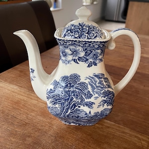 May include: A blue and white porcelain teapot with a floral design. The teapot has a lid and a handle. The teapot is sitting on a wooden table.