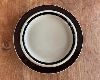 May include: A brown and black ceramic plate with a white center. The plate has a simple design with concentric circles.