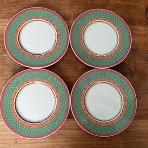 Op de afbeelding: Een set van vier ronde keramische borden met een wit midden, een brede groene rand met een goudkleurig ruitpatroon en een decoratieve binnenring met rode en gouden bloemmotieven, afgewerkt met een dunne rode rand langs de buitenkant.