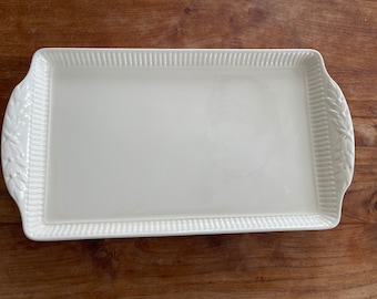 May include: A rectangular, off-white serving tray with a raised, ribbed border and decorative leaf accents on the handles. The tray is approximately 14 inches long and 9 inches wide, suitable for serving appetizers or desserts.