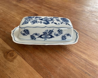 May include: A white porcelain butter dish with a blue and white floral design. The dish has a lid and a base.