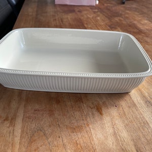Könnte beinhalten: Eine weiße Keramik-Backform mit geriffeltem Rand und einem Perlenrand. Die Form ist leer und bereit zum Backen.