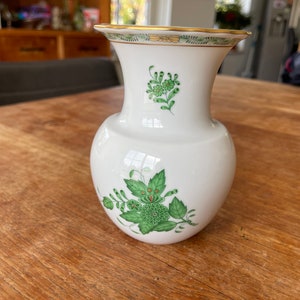 May include: A white porcelain vase with a green and gold floral design. The vase has a round body and a narrow neck.