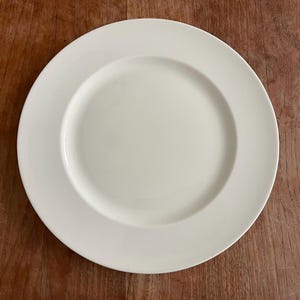 May include: A plain white ceramic dinner plate with a slightly raised rim.
