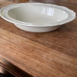 Puede incluir: Un tazón de cerámica blanco con un borde festoneado. El tazón está sobre una mesa de madera.