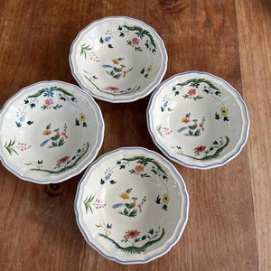 May include: Four white ceramic bowls with a floral and bird design. Each bowl features a scalloped edge with a blue trim. The interior of the bowls are decorated with colorful flowers and a bird.