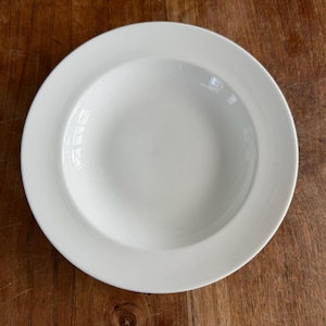 Pode incluir: Uma tigela de sopa redonda de cerâmica branca com uma borda larga e plana e um centro profundo e côncavo. A tigela apresenta um acabamento liso e brilhante e um design limpo, oferecendo uma peça neutra e versátil para servir vários pratos.