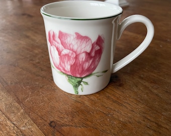 Puede incluir: Taza de cerámica blanca con un borde verde y una ilustración de una flor rosa.