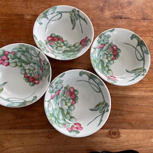 Peut inclure: Quatre bols en céramique blanche avec un motif de raisin vert et rose. Les bols sont disposés en cercle sur une surface en bois.