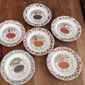 May include: A set of five round ceramic plates with scalloped edges, each featuring a central illustration of a fruit tart and a corresponding fruit tree. The plates display text labels including Tarte aux Cerises, Tarte aux Myrtilles, and Tarte aux Abricots, with colorful fruit motifs decorating the rims.
