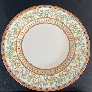 Op de afbeelding: Een wit keramiek dinerbord met een decoratieve rand met een herhalend patroon van groene bladeren, oranje fruit en blauwe en gouden geometrische vormen.