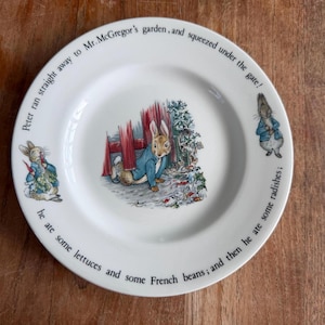 May include: White ceramic plate with illustrations of Peter Rabbit. The plate has text around the rim: "Peter ran straight away to Mr. McGregor's garden, and squeezed under the gate! He ate some lettuces and some French beans; and then he ate some radishes."