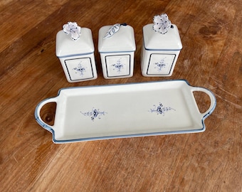 May include: Three white ceramic containers with blue floral designs and lids, sitting on a white tray with blue floral designs and handles.