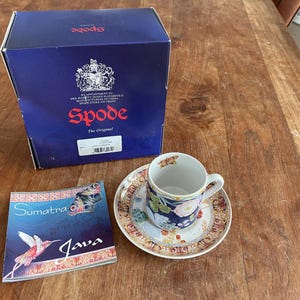 Op de afbeelding: Een blauw en wit theekopje en schotelset met een bloemenmotief. De schotel heeft een gouden rand. Het theekopje heeft een gouden handvat. De set is van het merk Spode. De doos voor de set is blauw en heeft het Spode-logo erop. De doos heeft ook de tekst "The Original".