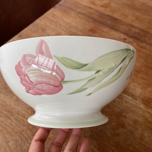 Op de afbeelding: Witte keramische kom met een roze tulpenontwerp. De kom heeft een afgeronde vorm en een voet. De tulp is geschilderd in roze en wit, met groene bladeren. Geschikt voor het serveren van voedsel, een decoratief item.
