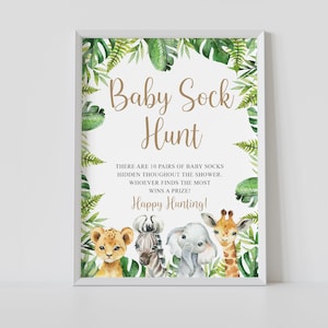 May include: A printable sign for a baby shower game called "Baby Sock Hunt". The sign features a jungle theme with green leaves, a lion, zebra, elephant, and giraffe. The text on the sign reads: "There are 10 pairs of baby socks hidden throughout the shower. Whoever finds the most wins a prize! Happy Hunting!"