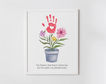 May include: A framed print with a watercolor illustration of a flower pot with a handprint in the center and flowers growing from it. The text below the image reads "The flowers that bloom tomorrow are the seeds you planted today."