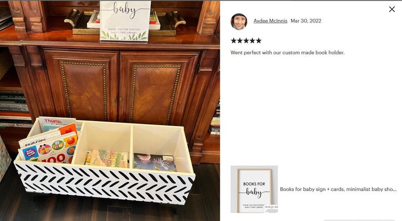 May include: A white and black chevron patterned book organizer with three compartments, filled with colorful children's books. A sign that says "baby" is on top of a wooden cabinet.
