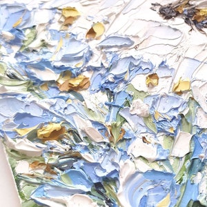 May include: A close-up of a painting depicting a cluster of blue and white flowers with yellow centers. The flowers are painted in a thick, textured style, giving the impression of brushstrokes.