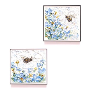 May include: Two framed paintings of bees flying near blue flowers. The paintings are on a white background.