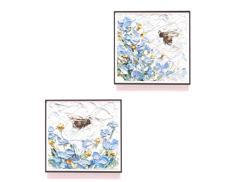 May include: Two framed paintings of bees flying near blue flowers. The paintings are on a white background.