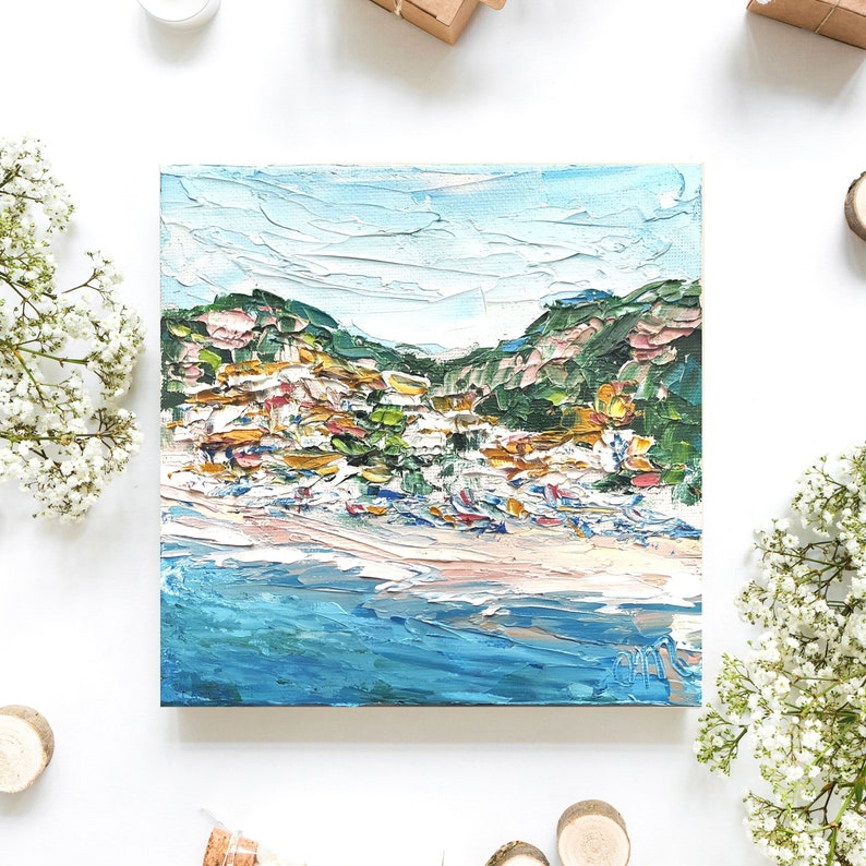 May include: A painting of a coastal town with colorful buildings on a hillside overlooking a blue ocean. The sky is a light blue with white clouds. The painting is done in a loose, impressionistic style.