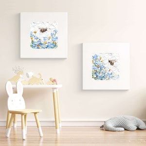 May include: Two framed paintings of blue flowers with bees flying around them. The paintings are hanging on a white wall in a room with a wooden table and chair.
