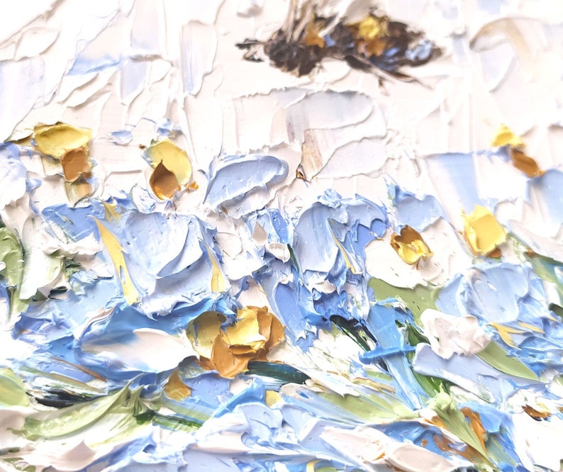 May include: A close-up of an oil painting depicting a field of blue and white flowers with yellow centers. The flowers are painted with thick, textured strokes of paint, giving the painting a three-dimensional effect.
