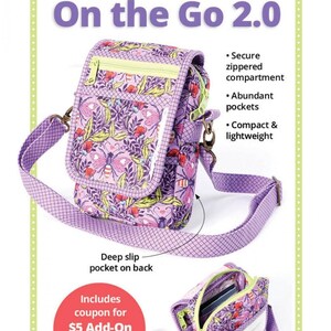 May include: Purple and green floral print crossbody bag with a zippered compartment, a deep slip pocket on the back, and a clear plastic window. The bag is labeled "On the Go 2.0" and includes a coupon for a $5 video tutorial.