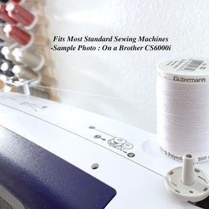Pode incluir: Uma m&aacute;quina de costura branca com um carretel de linha de poli&eacute;ster branca G&uuml;termann colocado em cima. A m&aacute;quina apresenta diagramas de enfiamento impressos e o texto: Fits Most Standard Sewing Machines -Sample Photo : On a Brother CS6000i.