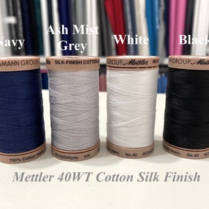 May include: Four spools of Mettler 40WT Cotton Silk Finish thread in navy, ash mist grey, white, and black. Each spool is labeled with the Mettler logo and the thread weight and type.
