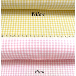Puede incluir: Dos rollos de tela de cuadros vichy, uno amarillo y otro rosa, cada uno con un patr&oacute;n de cuadros peque&ntilde;os. Una regla es visible a lo largo del borde inferior de la tela amarilla, mostrando marcas en cent&iacute;metros para escala y medida.