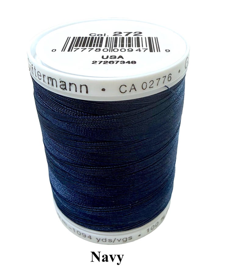 Pode incluir: Um carretel de linha de costura azul-marinho da marca G&uuml;termann. A etiqueta superior branca exibe o texto Col. 272, um c&oacute;digo de barras, USA e 27267348. A lateral apresenta o nome G&uuml;termann e CA 02776. A etiqueta inferior indica 1094 yds/vgs.