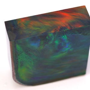May include: A rectangular block of polished gemstone, showcasing a vibrant display of colors. The top surface features streaks of red and orange, transitioning into green and blue hues. The gemstone has a glossy finish.