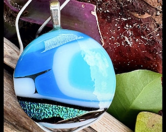 Round circle glass pendant with a medley of blues hints of sparkle,white, black and dichroic accents and shimmering iridescent glass.