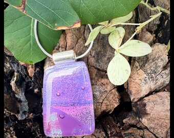 Glass pendant is a rectangular shape. Colors are a variety of sparkling purples with a dichroic essence.