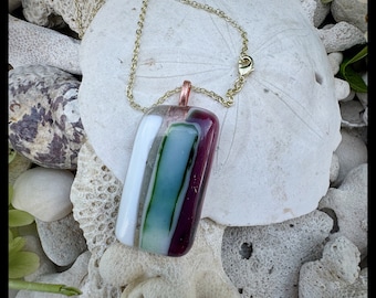Glass pendant is a medley of colors  transparent clear shimmering with  greens and an array of purples opaque while reflecting light.
