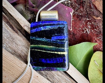 Hand made glass pendant. Fused by artist. Shimmering dichroic blues and purples with iridescent accents. Gold wave runs through.