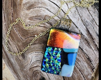 Glass pendant is a rectangle shape. Colors are a variety of sparkling blue and greens with a dichroic essence.