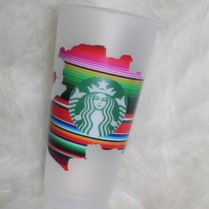 May include: A white frosted tumbler with a green Starbucks logo and a colorful serape design.