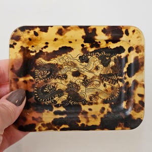 Op de afbeelding: Rechthoekige sieradenschaal met een schildpadpatroon. De schaal heeft een gedetailleerd drakenontwerp in het midden. De kleuren van de schaal zijn bruin, beige en zwart.