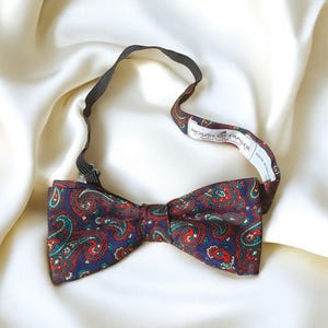May include: A paisley patterned bow tie with a black elastic band. The bow tie has a red, green, and blue paisley pattern on a dark blue background. The bow tie has a label that reads "House of Fraser" and "Made in England".