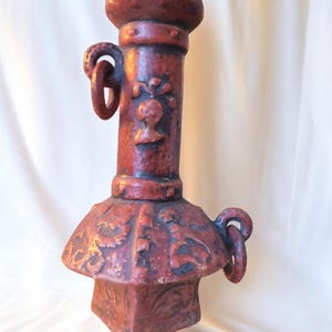 Könnte beinhalten: Ein rotes Keramikgewicht mit aufwendigen Schnitzereien und einem Ring oben. Das Gewicht ist pagodenförmig mit abgerundeter Spitze.