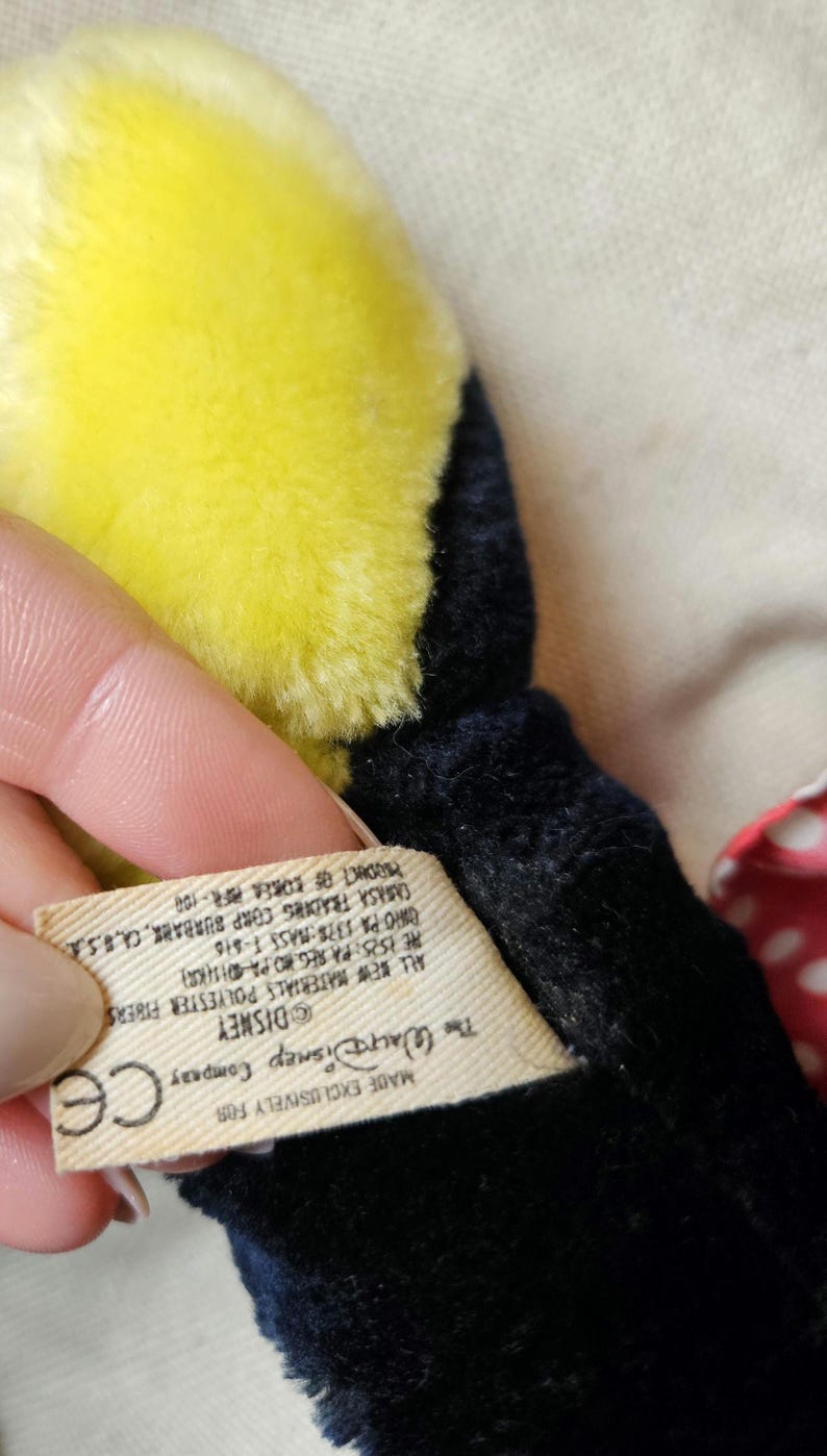 May include: A black and yellow plush toy with a white tag that reads "Made Exclusively For The Walt Disney Company Disney CE All New Materials Polyester Fibers HE ISIS: PA REGNO PA DISKR ORO PA 1378 MASS T-810 CARASA TRADING CORP SURBANK, CA, B.S PRODUCT OF KOREA PIR-100"